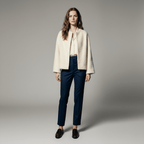 Woman wearing a cream jacket and blue pants on a gray background
