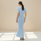 Woman wearing a light blue ribbed dress against a beige wall.