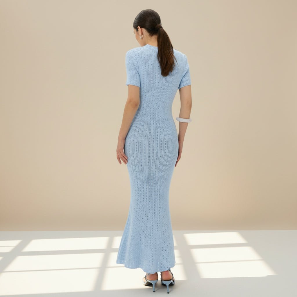 Woman wearing a light blue ribbed dress against a beige wall.