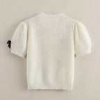 White knit sweater with a black tag on a beige background