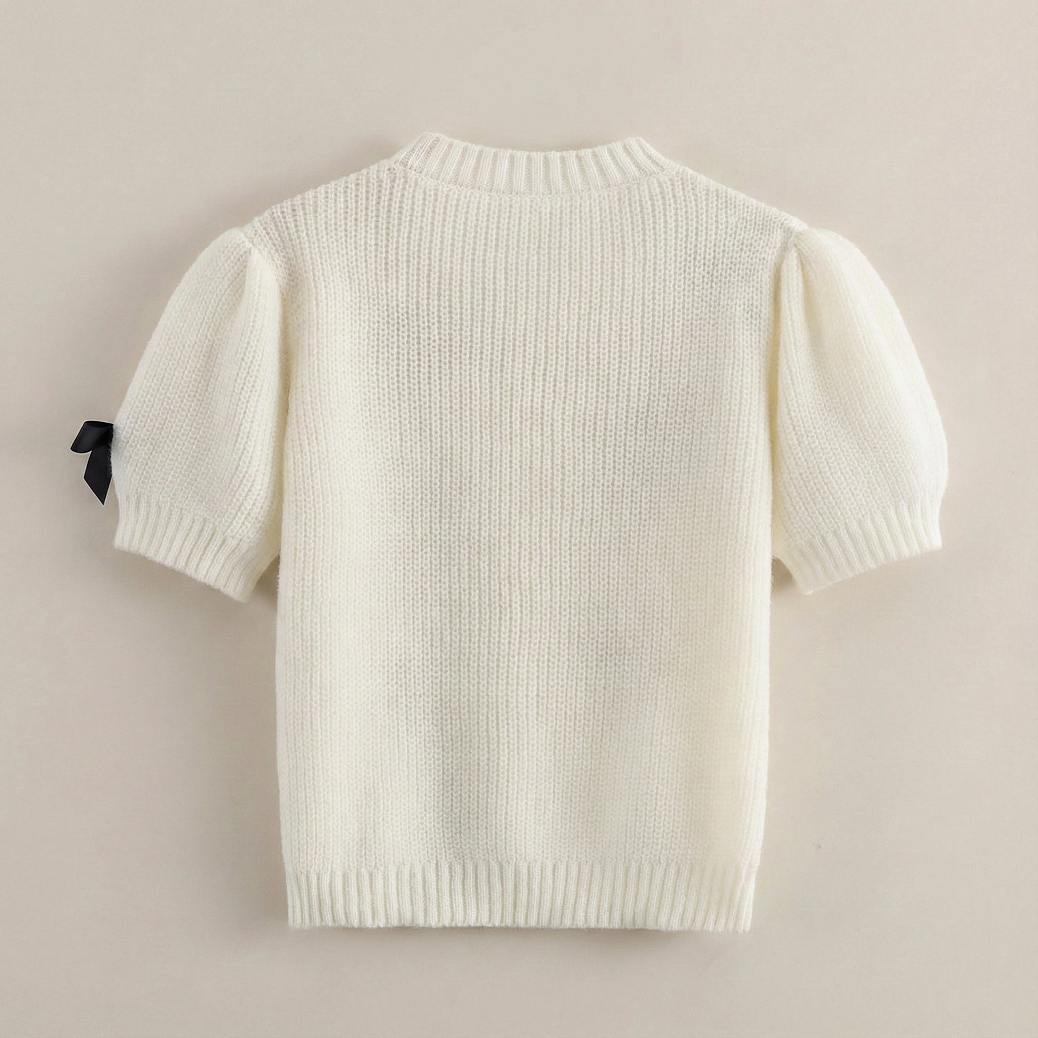 White knit sweater with a black tag on a beige background