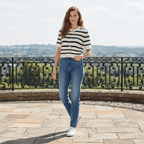 Woman wearing a striped shirt and jeans standing on a stone path with a scenic background