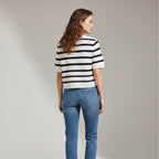 Woman wearing a black and white striped shirt and blue jeans on a plain background