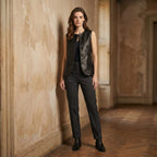 Woman in a black sleeveless top and pants standing against a textured wall.