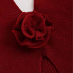 Close-up of a red knitted garment with a flower detail on a plain background
