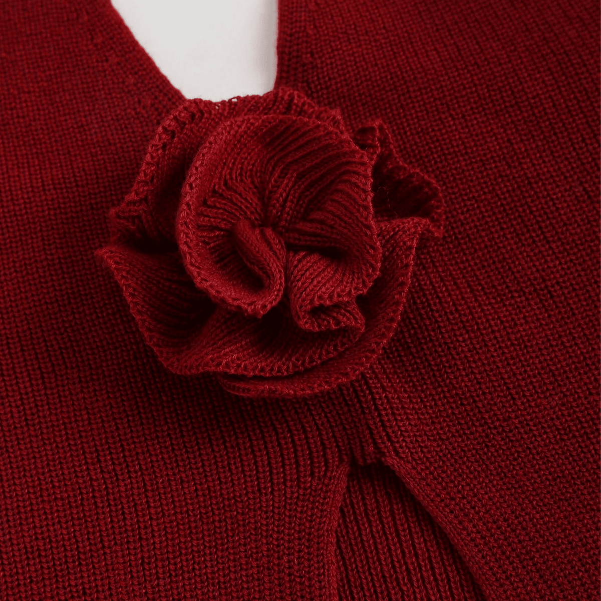 Close-up of a red knitted garment with a flower detail on a plain background