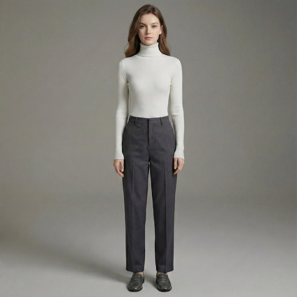 Woman wearing a white turtleneck and gray pants against a plain background