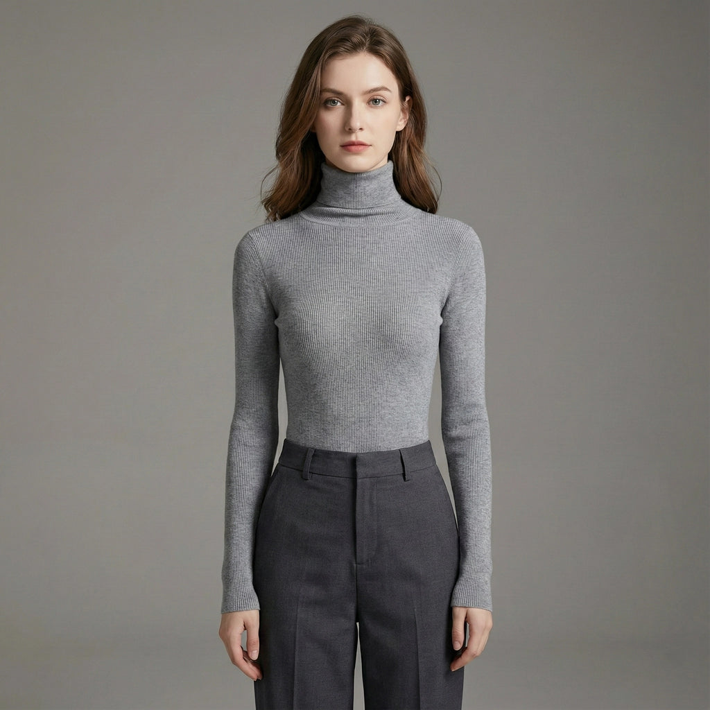 Woman wearing a gray turtleneck sweater and dark pants against a plain background