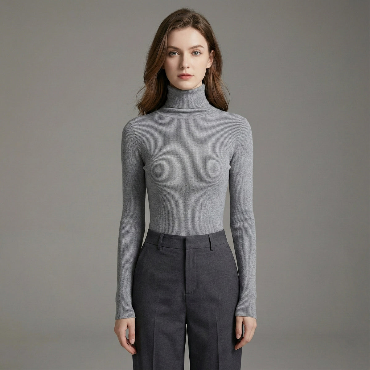 Woman wearing a gray turtleneck sweater and dark pants against a plain background