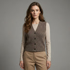 Woman wearing a brown knitted vest over a beige long-sleeve shirt and beige pants on a gray background
