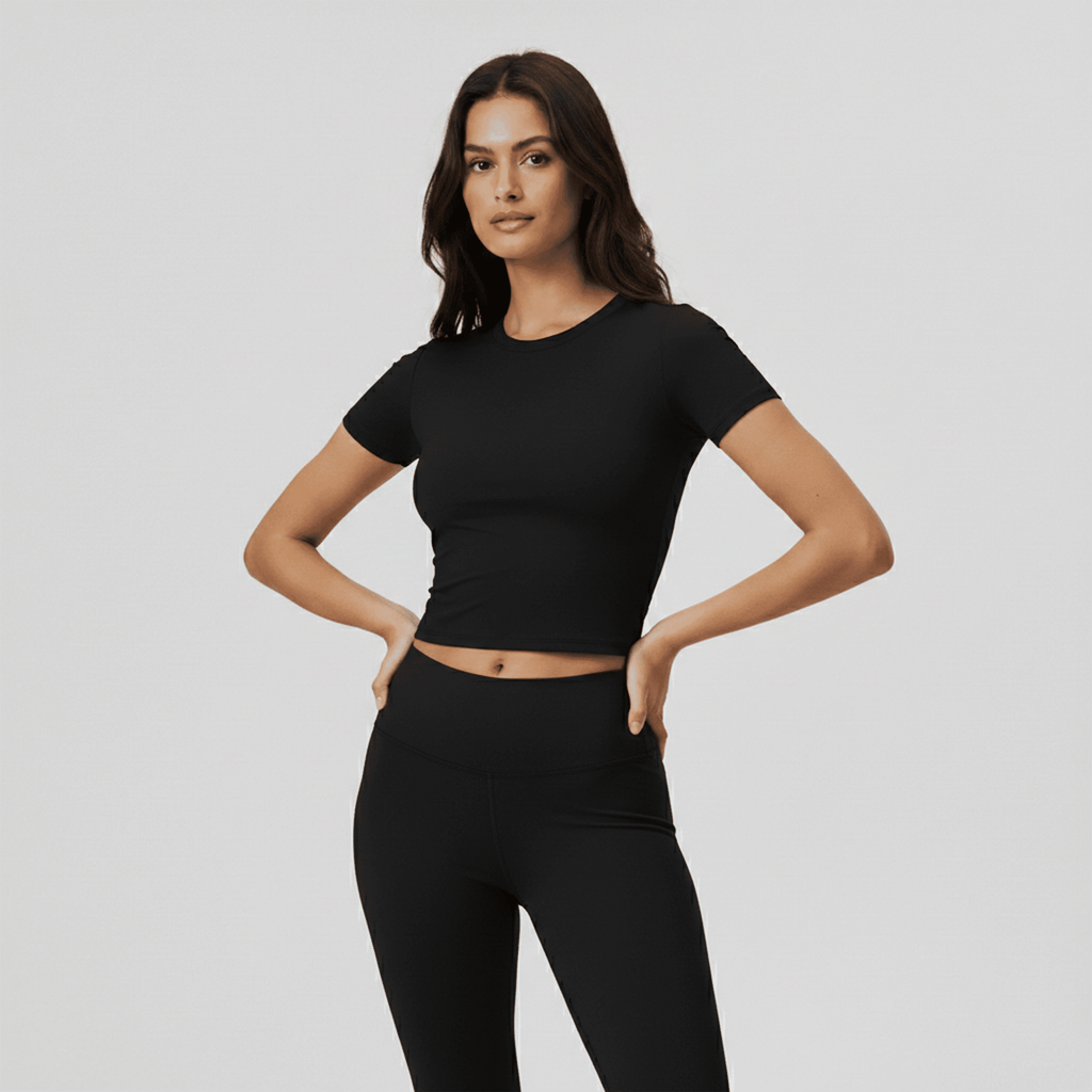 Woman wearing a black crop top and leggings on a light gray background