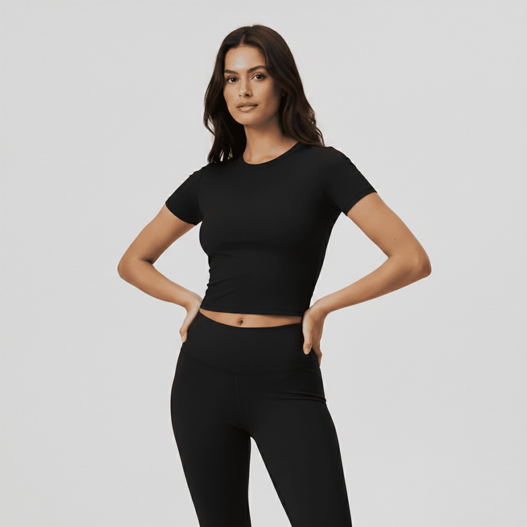 Woman wearing a black crop top and leggings on a light gray background