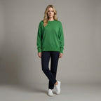 Woman wearing a green sweater and navy pants against a gray background