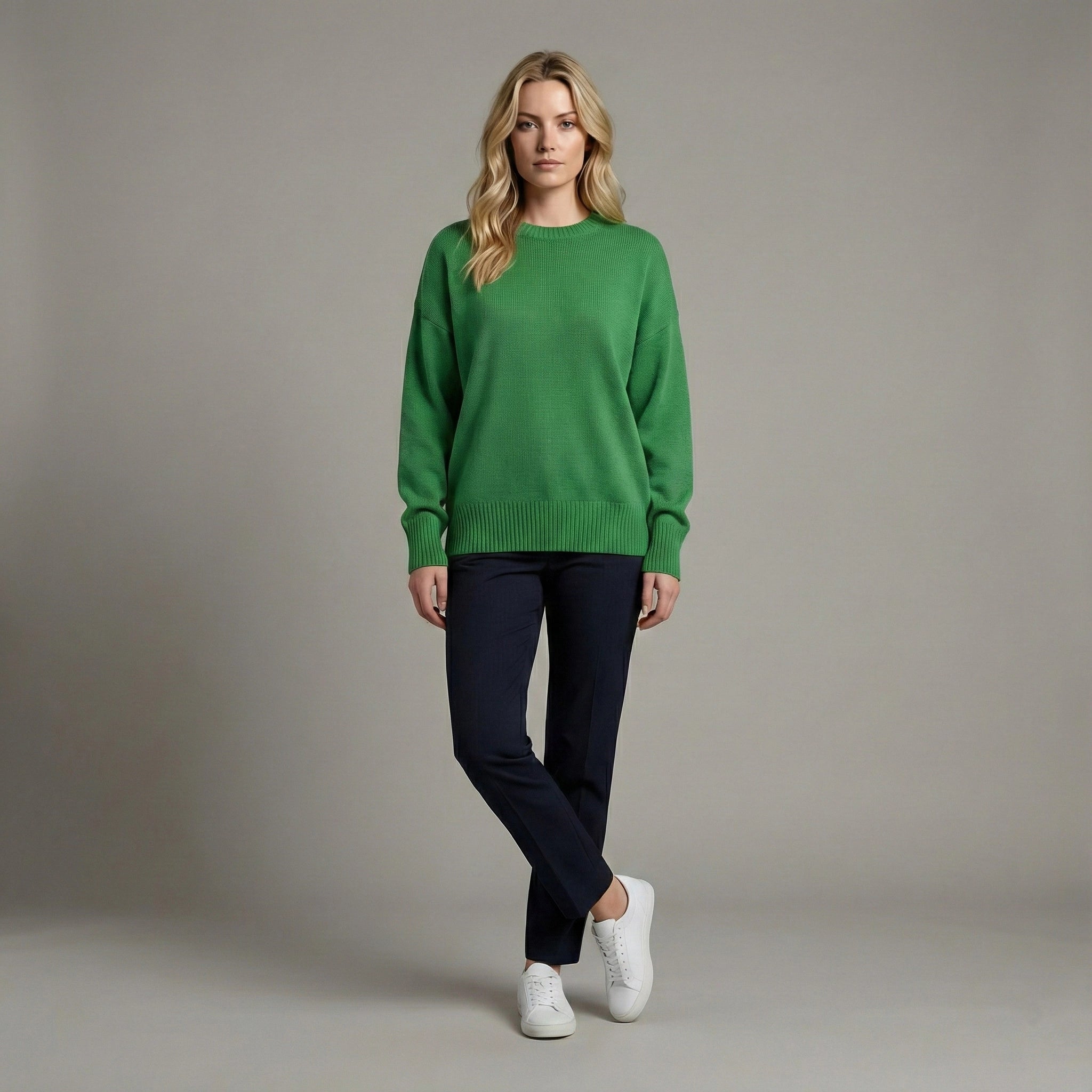 Woman wearing a green sweater and navy pants against a gray background