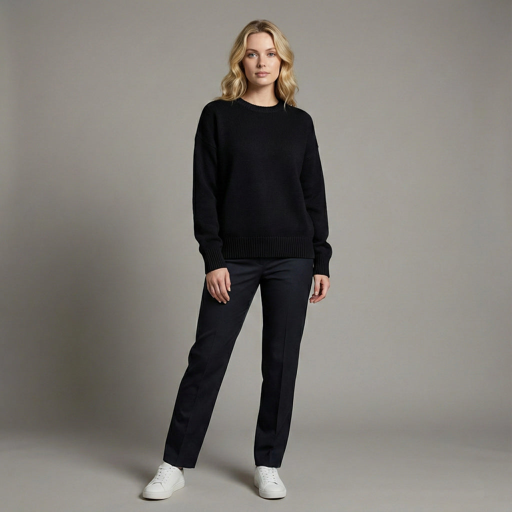 Woman wearing a black sweater and pants with white shoes on a gray background