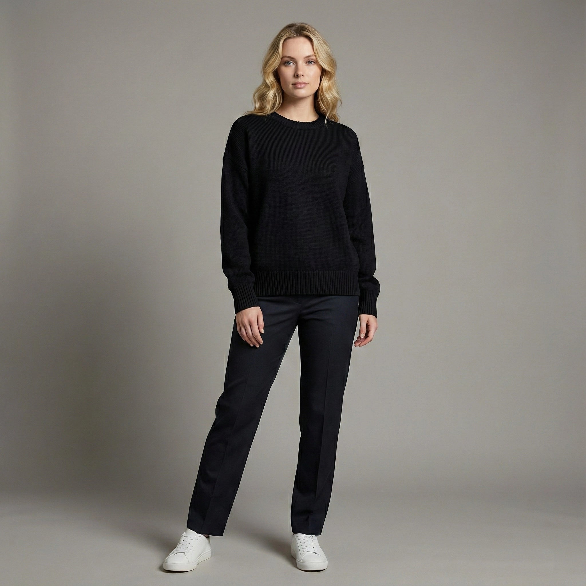 Woman wearing a black sweater and pants with white shoes on a gray background