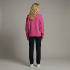 Woman wearing a pink sweater and black pants against a neutral background