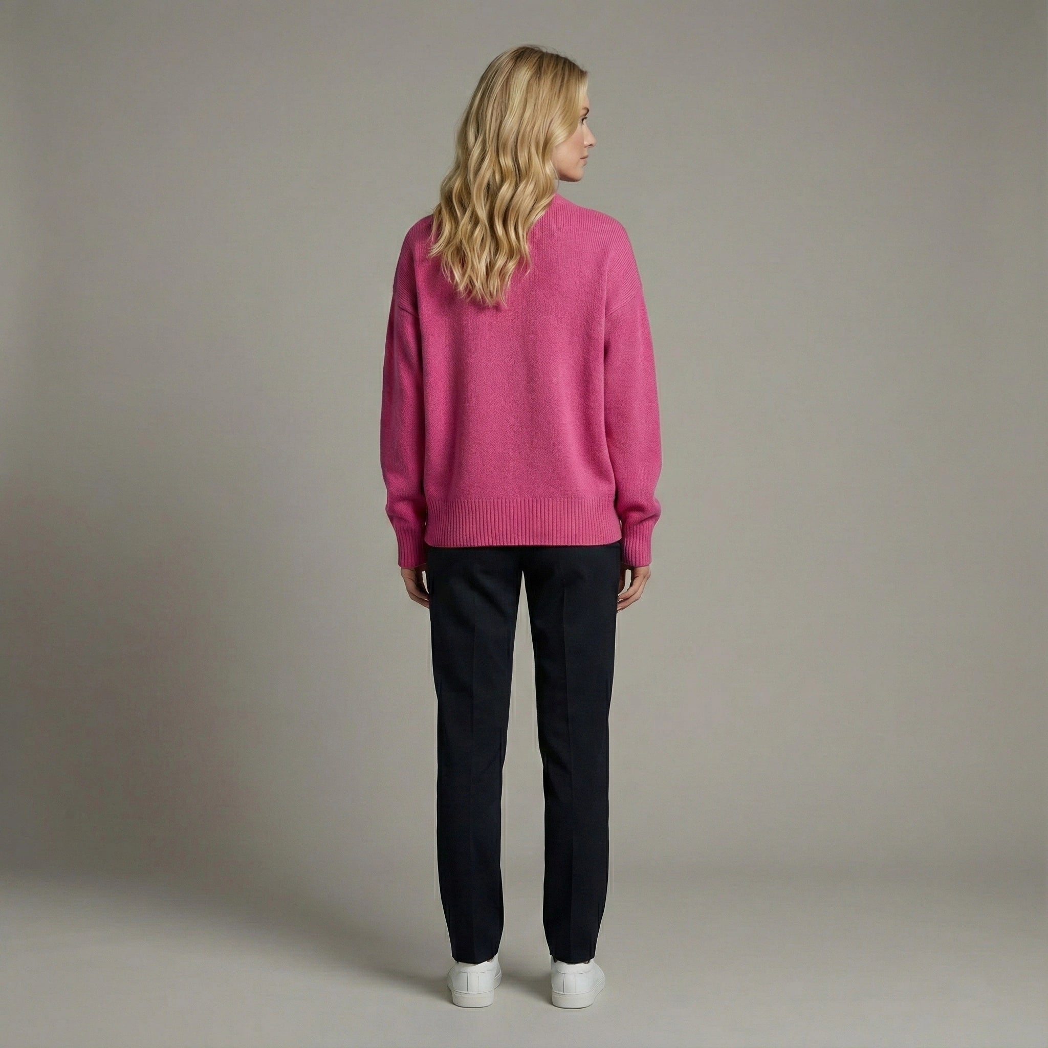 Woman wearing a pink sweater and black pants against a neutral background