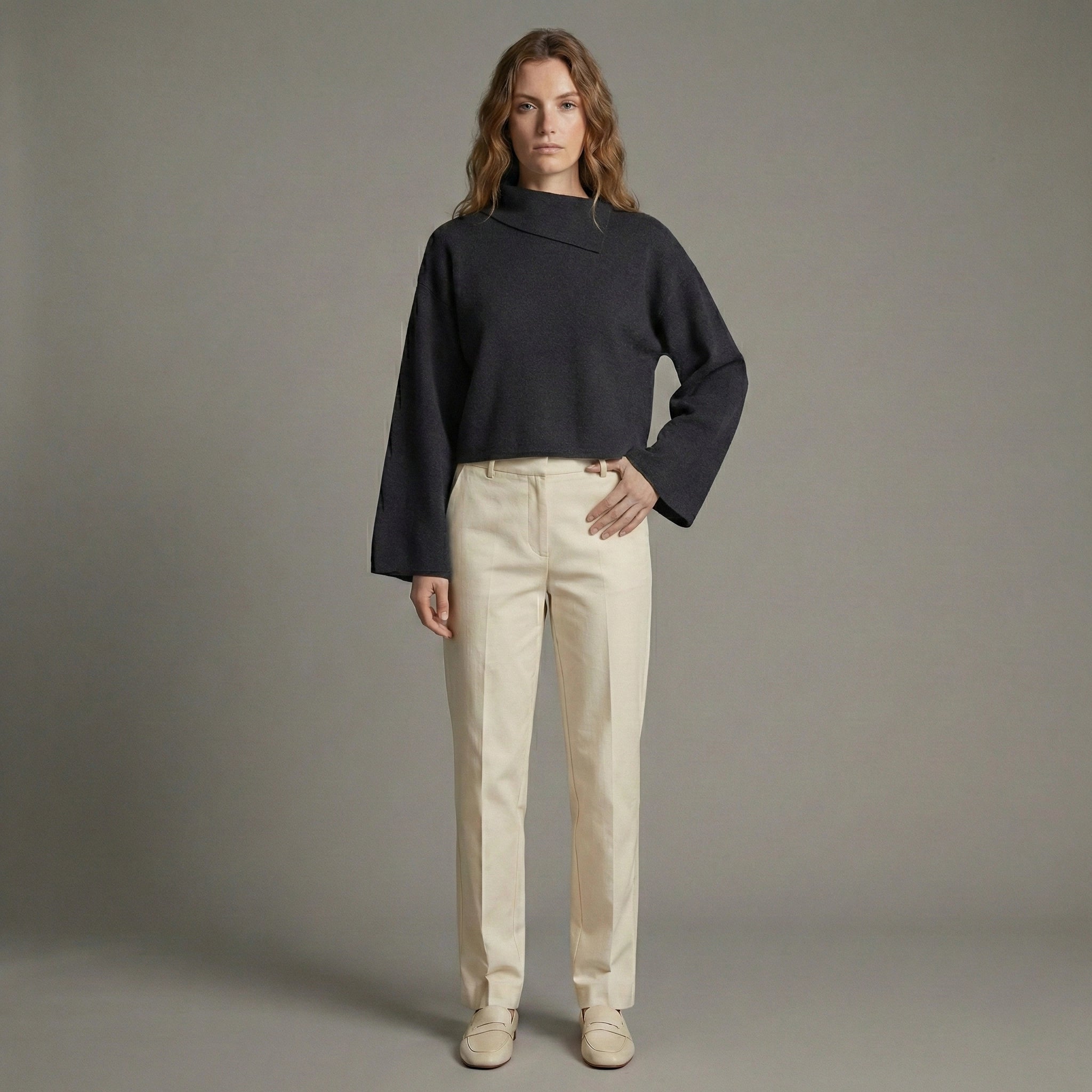 Woman wearing a black sweater and beige pants against a gray background