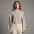 Woman wearing a beige sweater and pants against a gray background