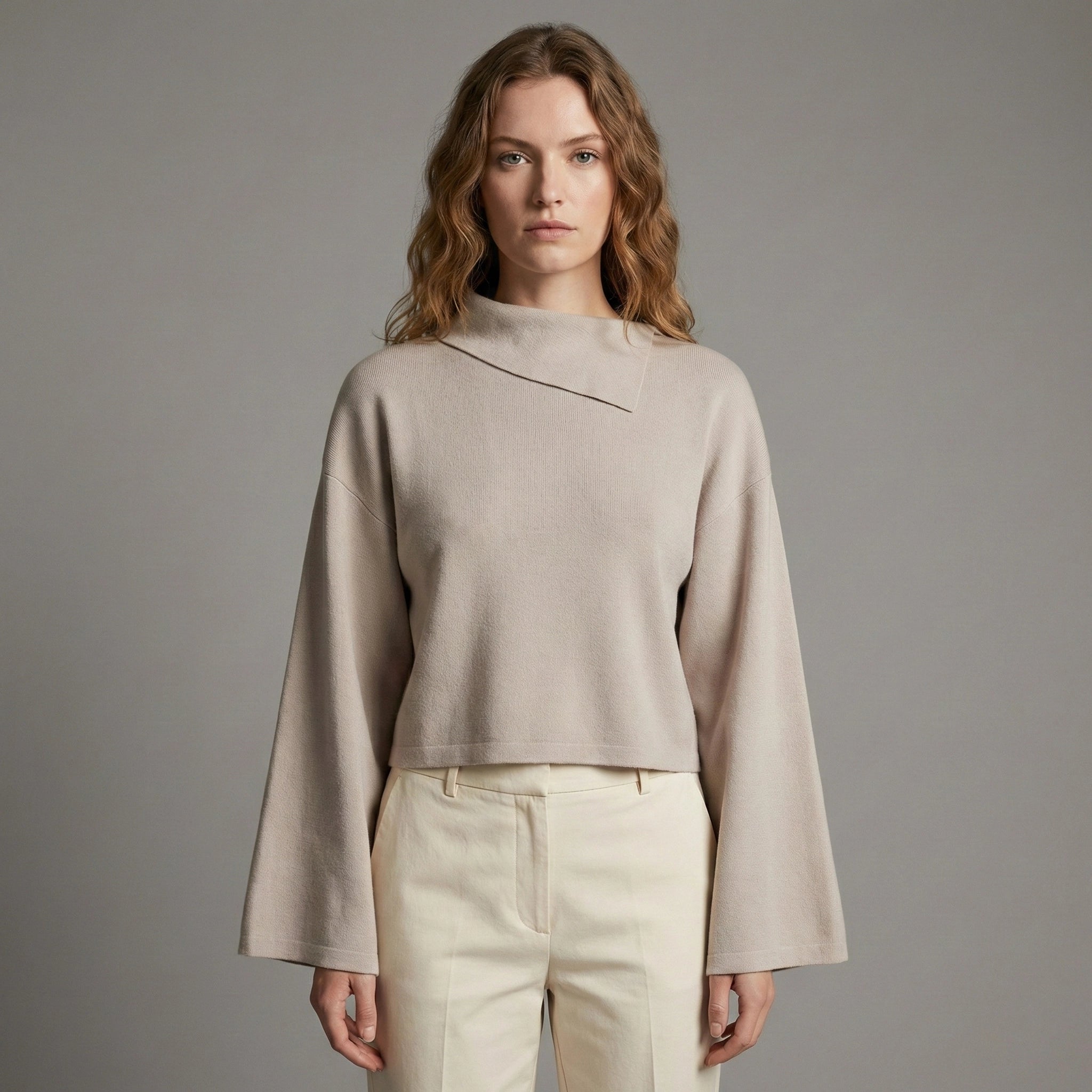 Woman wearing a beige sweater and pants against a gray background