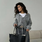 Woman wearing a gray cardigan holding a black handbag against a neutral background