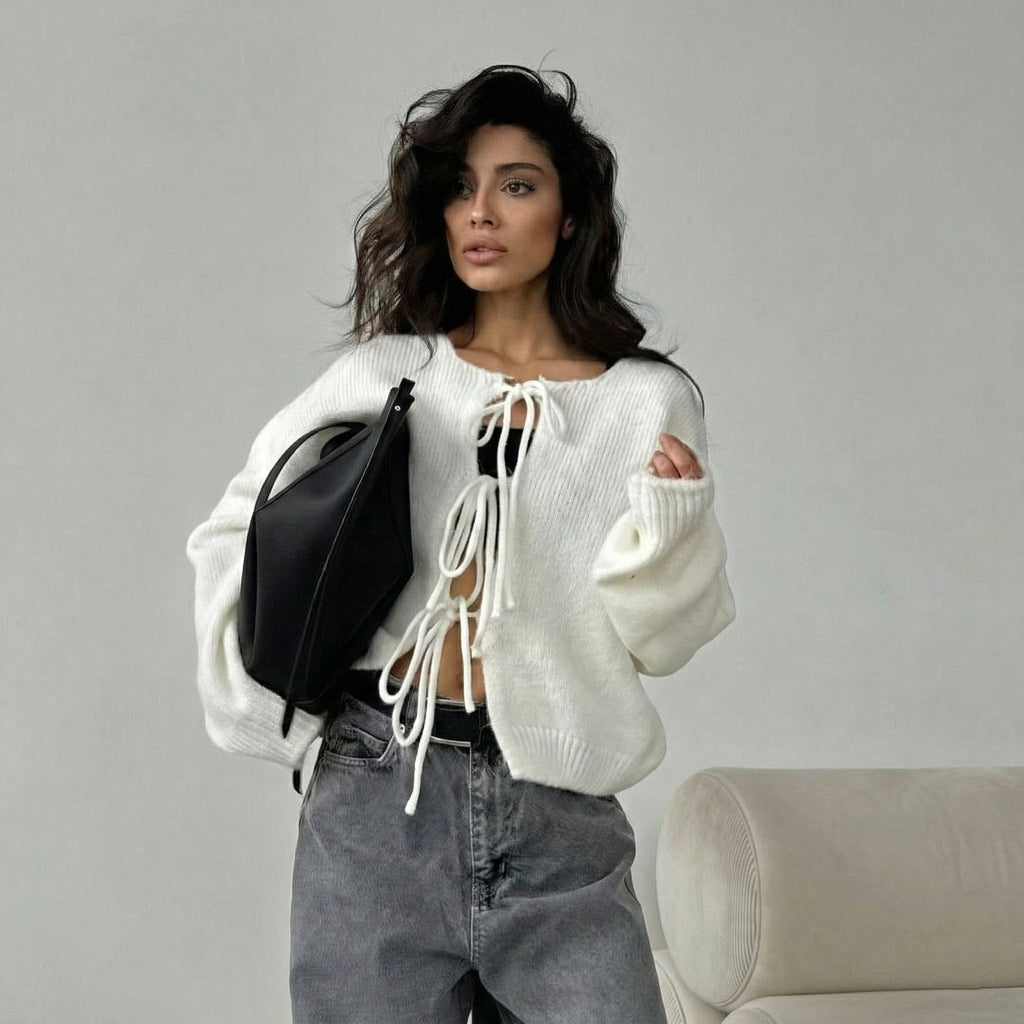 Woman wearing a white sweater with a black bag against a gray background