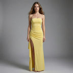 Woman wearing a strapless yellow evening gown with a slit on a gray background
