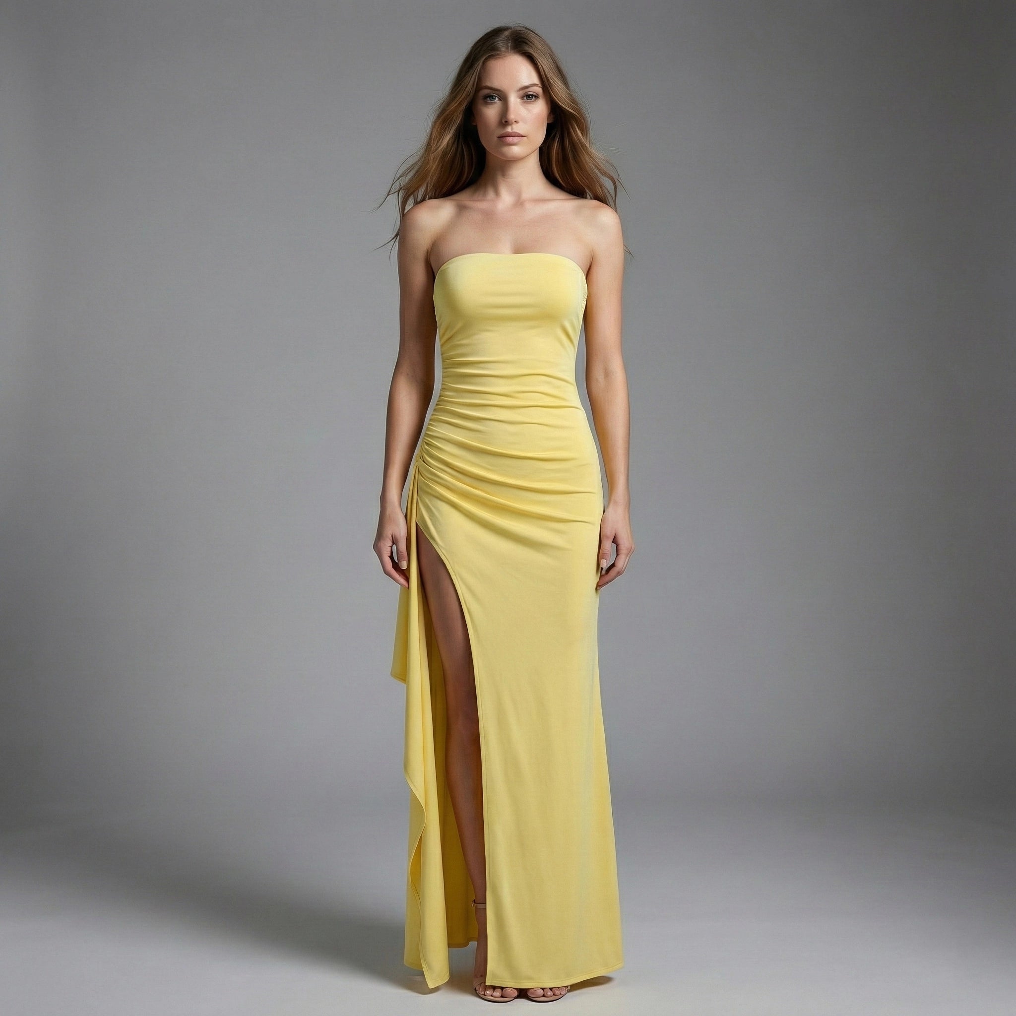 Woman wearing a strapless yellow evening gown with a slit on a gray background