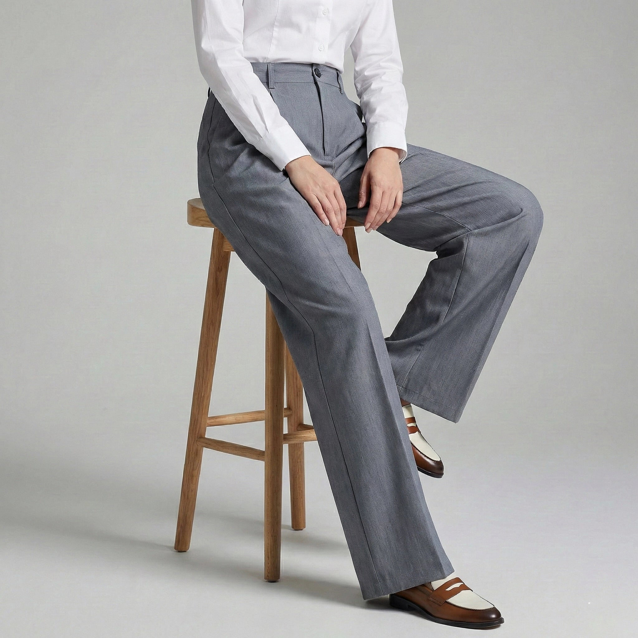 Person wearing gray wide-leg pants sitting on a wooden stool against a plain background
