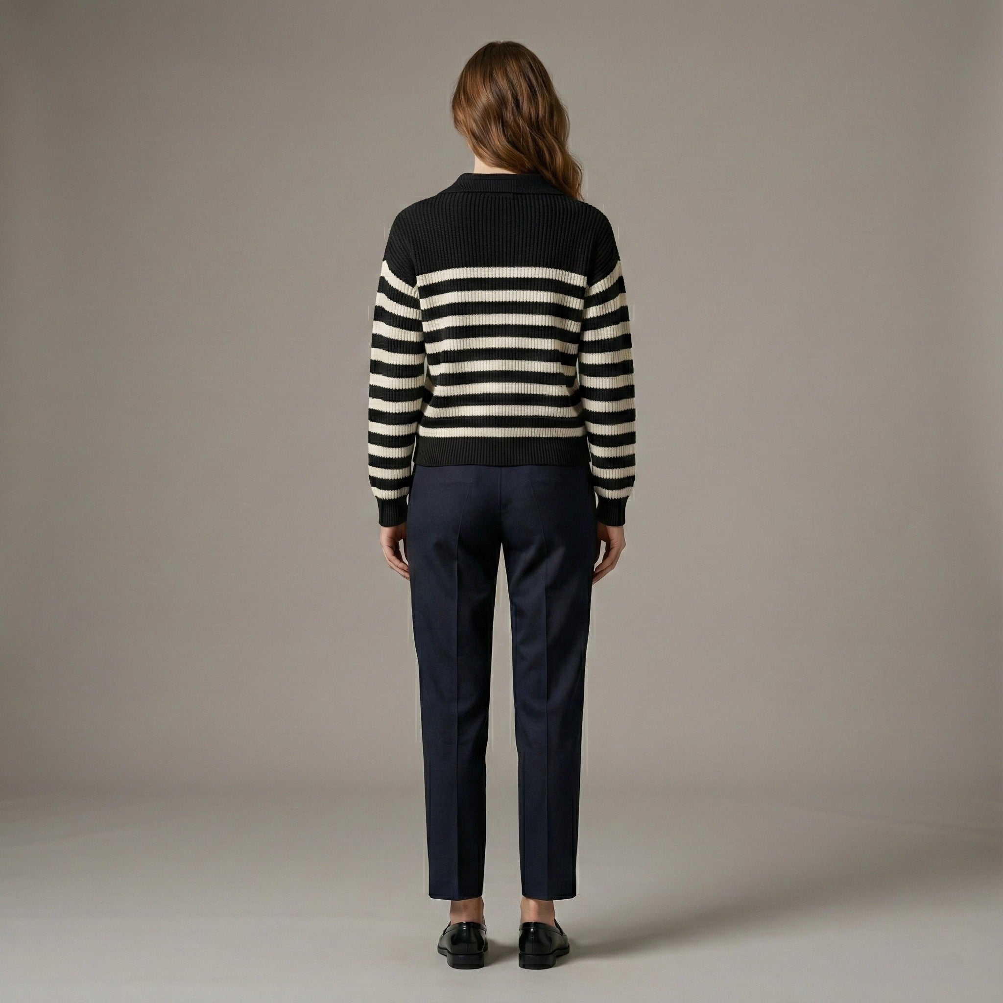 Person wearing a black and white striped sweater and dark pants against a plain background