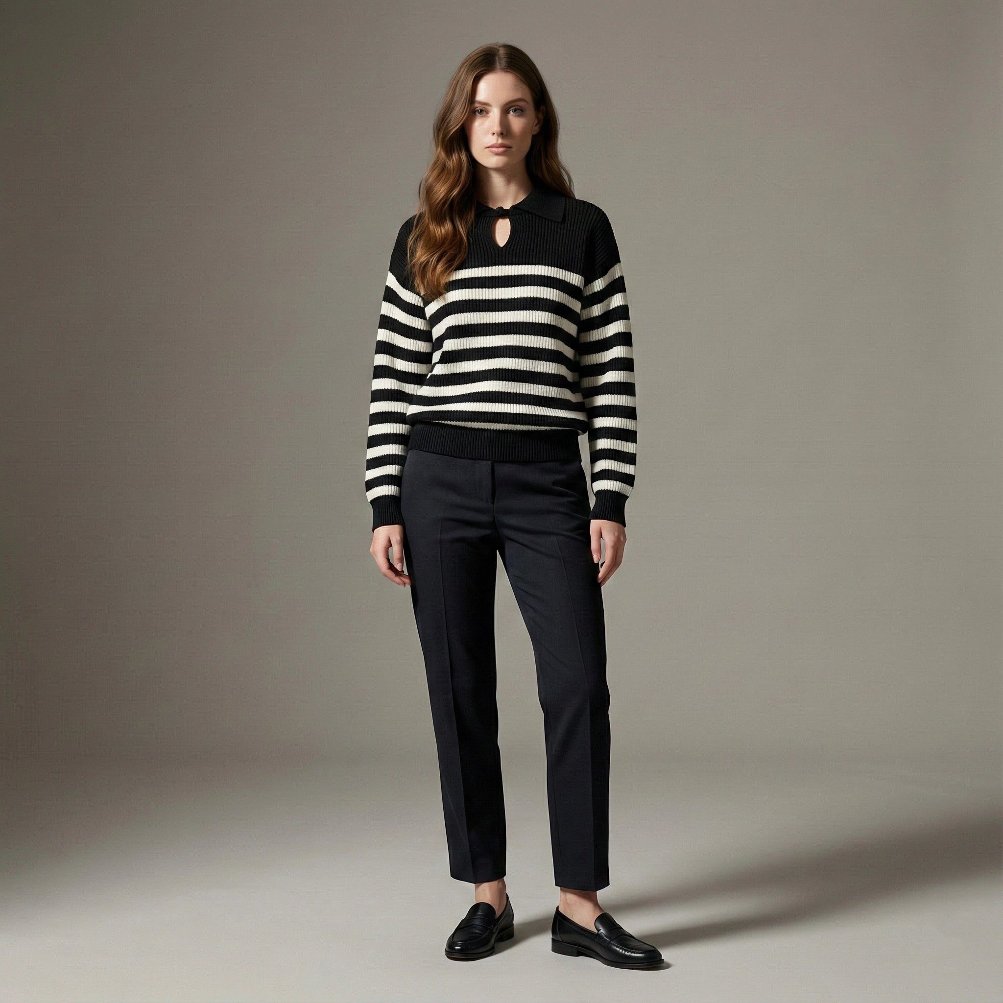 Woman wearing a black and white striped sweater with black pants against a neutral background