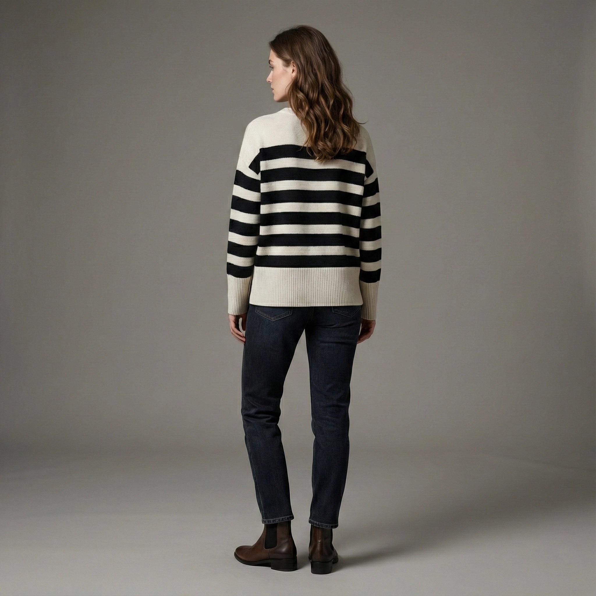 Woman wearing a black and white striped sweater and dark jeans on a gray background