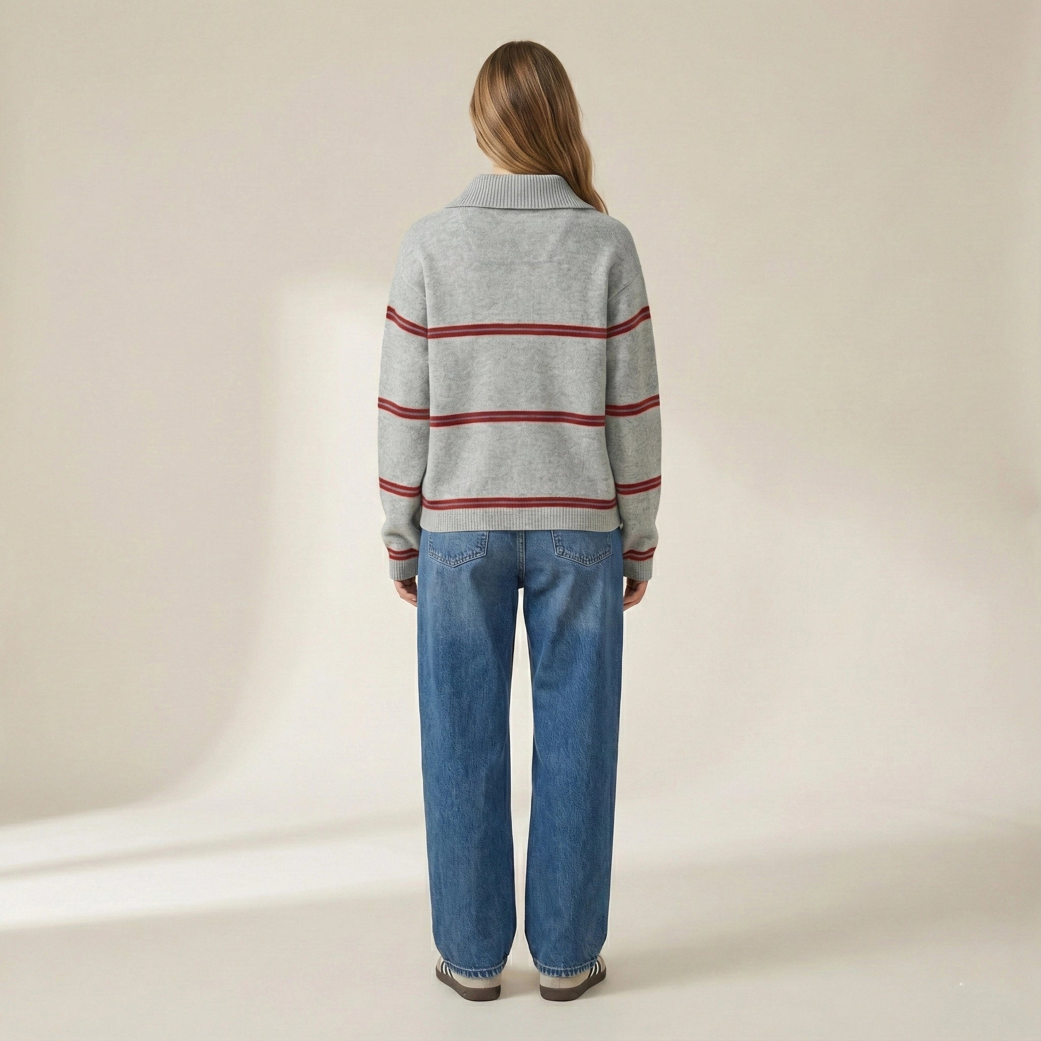 Person wearing a gray sweater with red stripes and blue jeans on a beige background