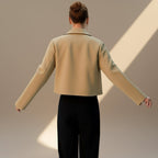 Person wearing a beige jacket and black pants against a neutral background
