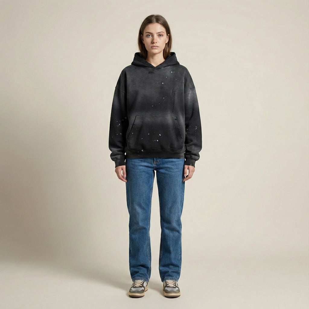 Person wearing a black hoodie and blue jeans on a beige background