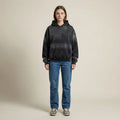 Person wearing a black hoodie and blue jeans on a beige background