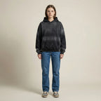 Person wearing a black hoodie and blue jeans on a beige background