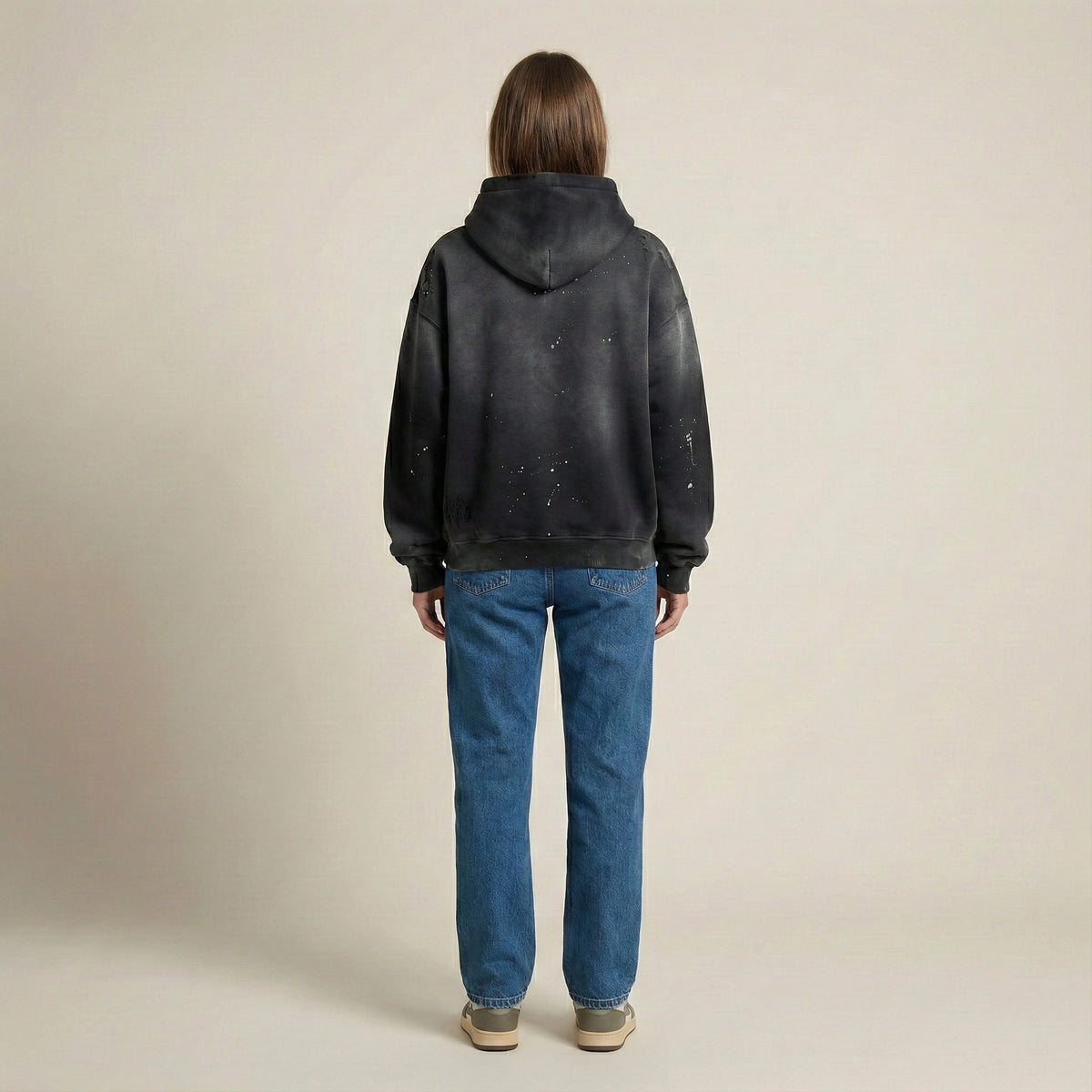 Person wearing a black hoodie and blue jeans on a beige background
