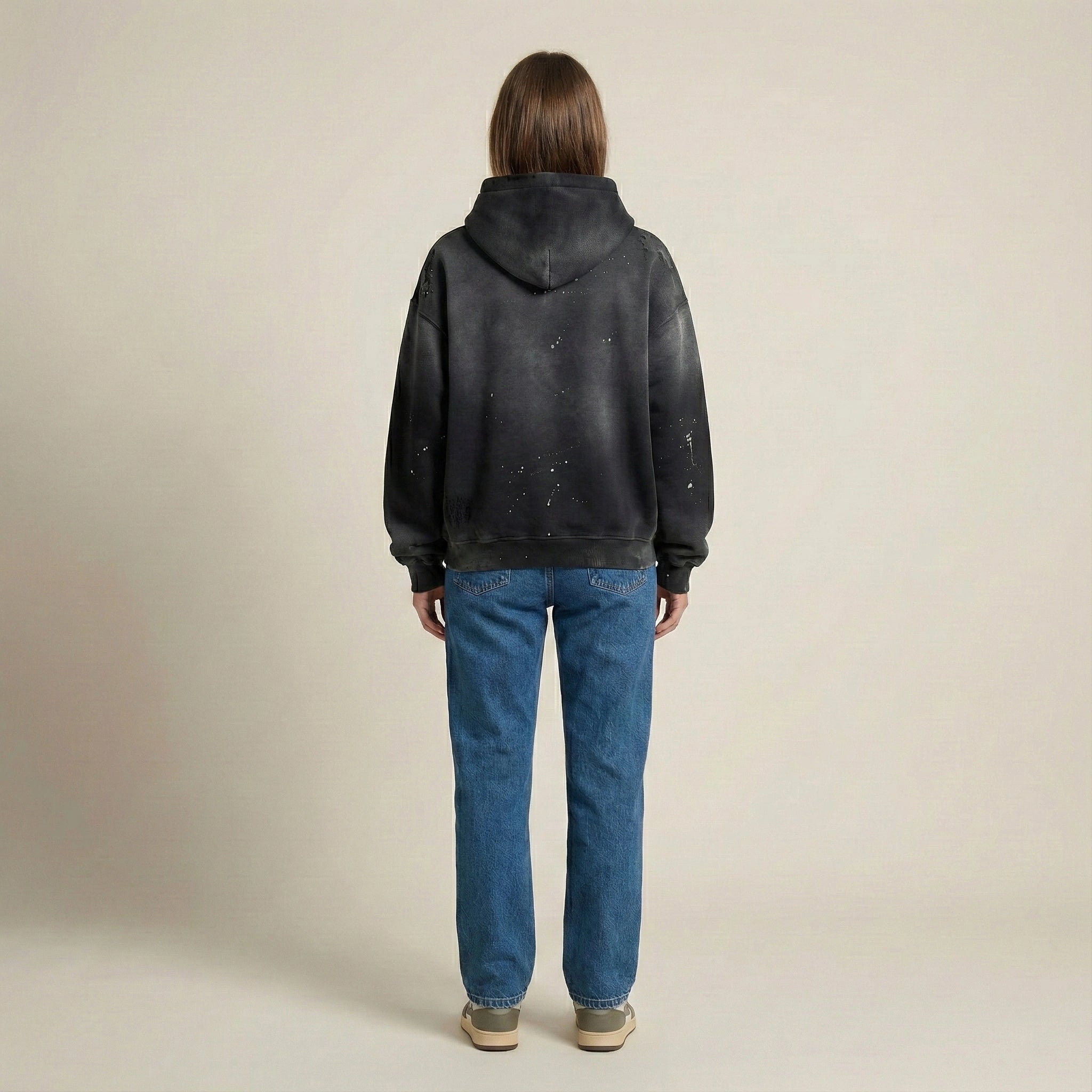 Person wearing a black hoodie and blue jeans on a beige background