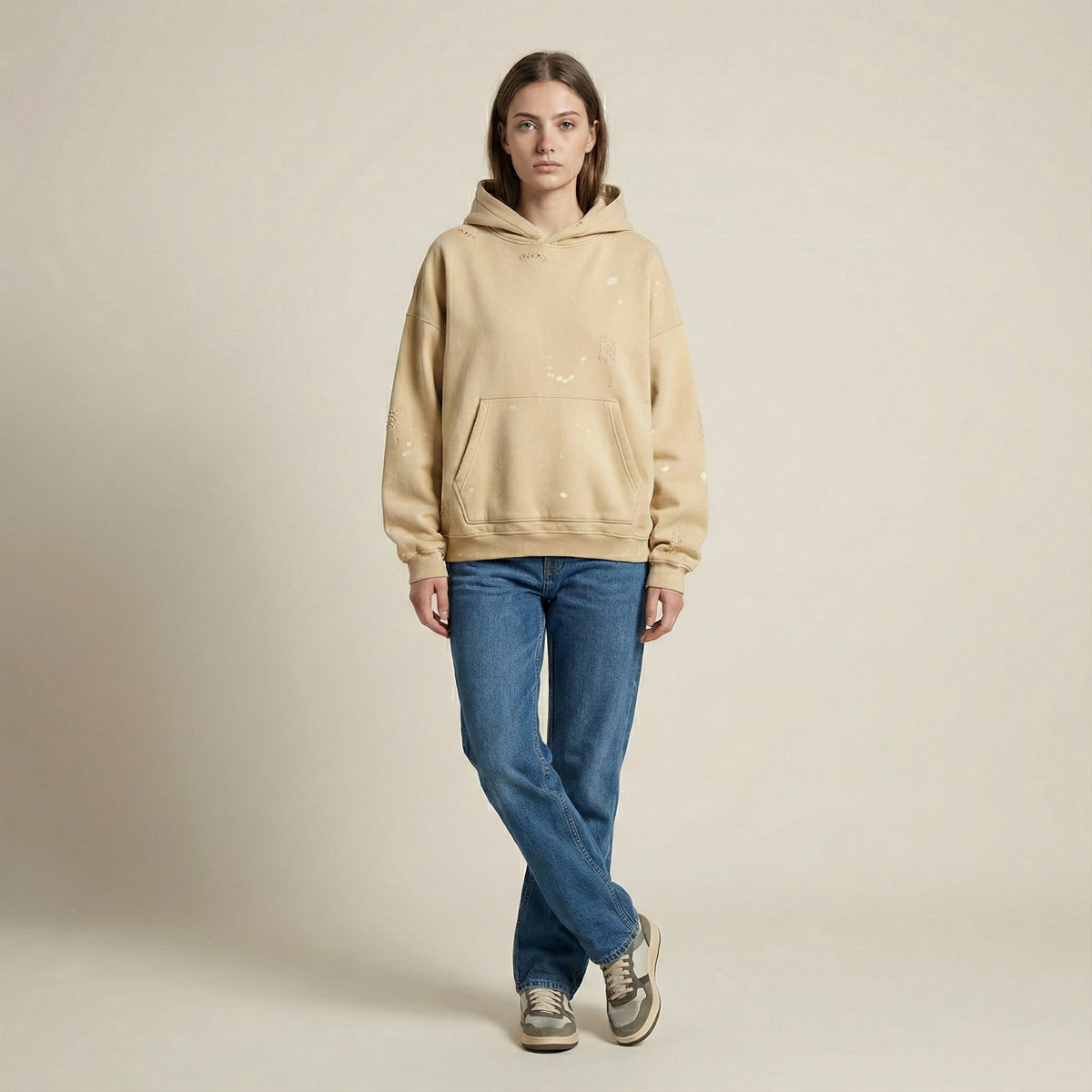 Person wearing a beige hoodie and blue jeans on a plain background