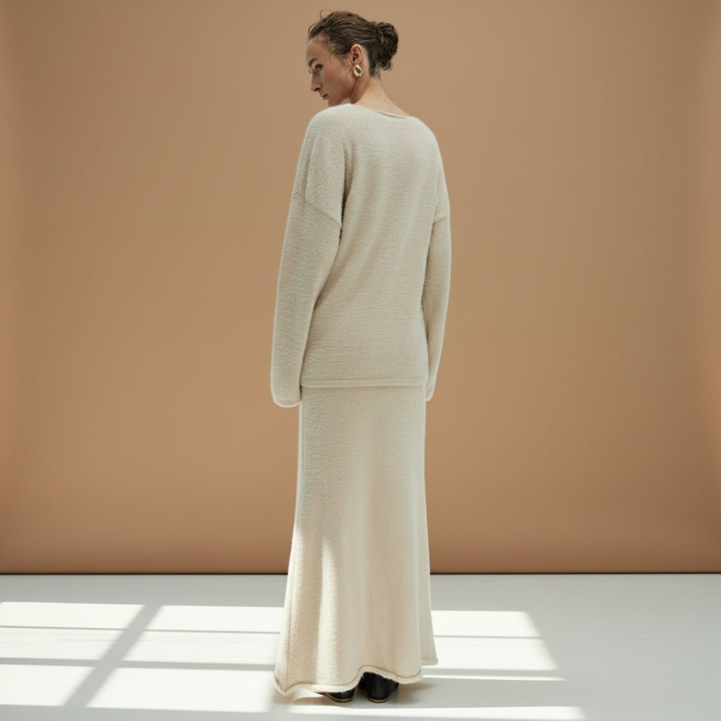 Person wearing a beige long-sleeve top and skirt set on a plain background