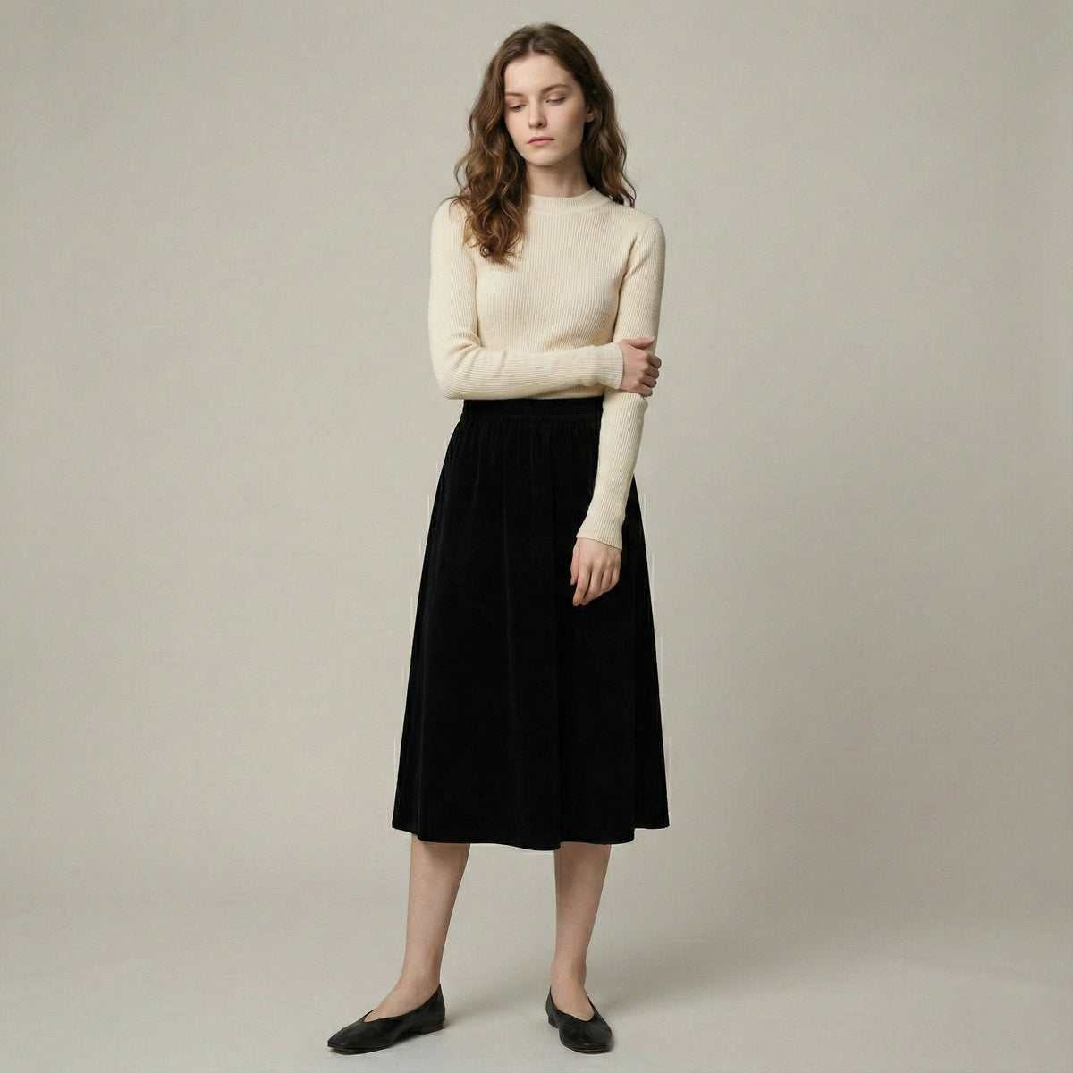 Woman wearing a beige sweater and black skirt against a plain background