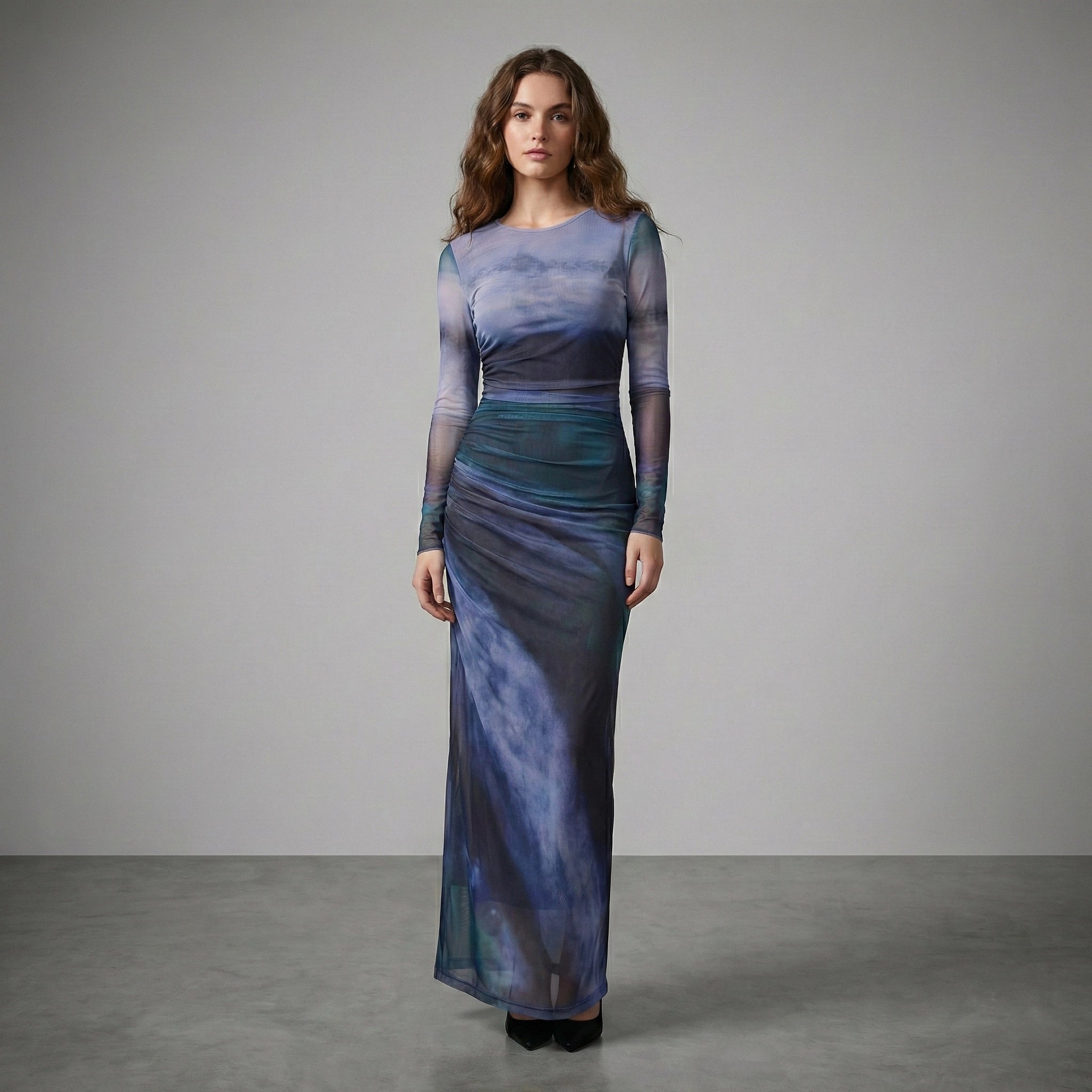 Woman wearing a long, sheer dress with a gradient of blue and purple colors on a gray background.