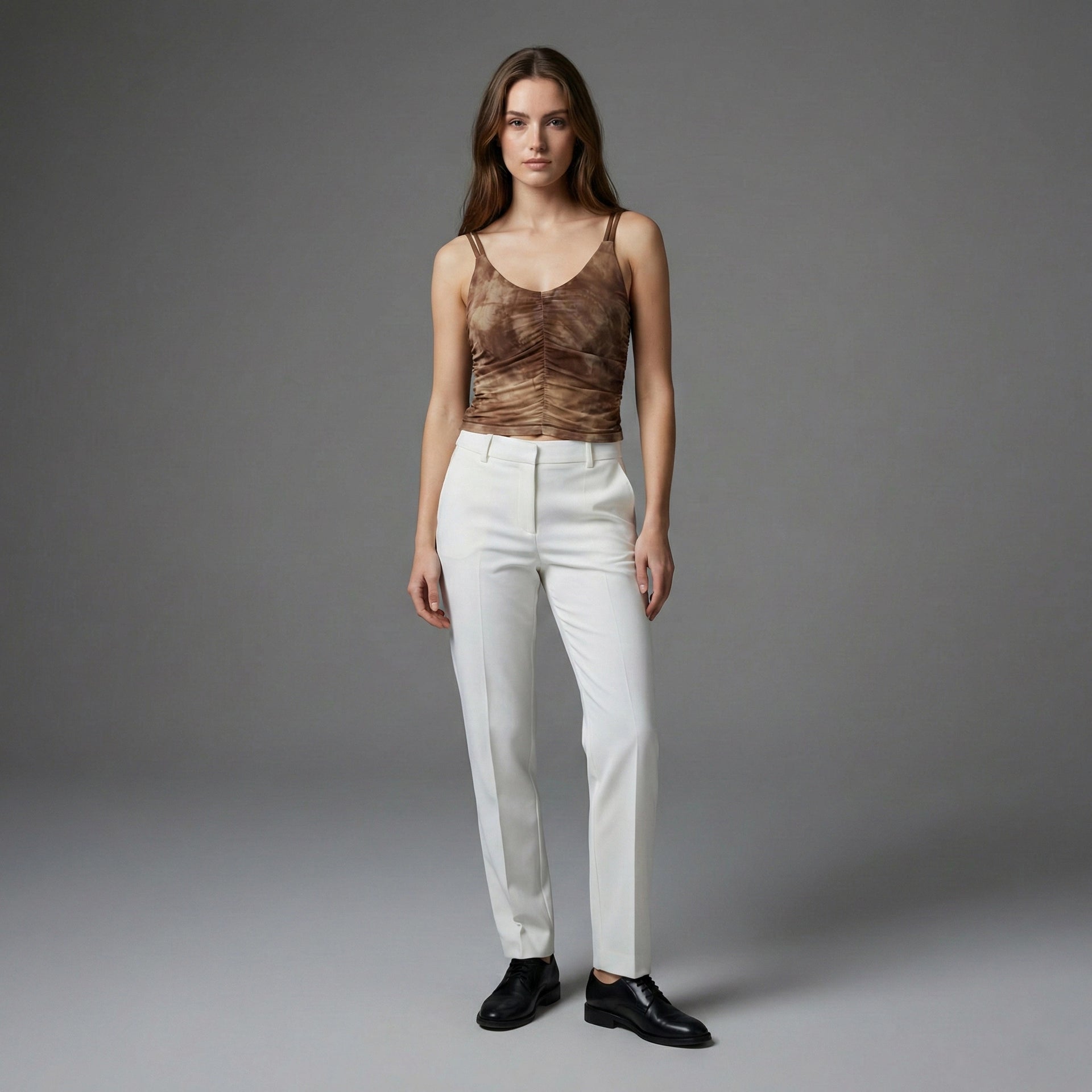 Woman wearing a brown top and white pants against a gray background