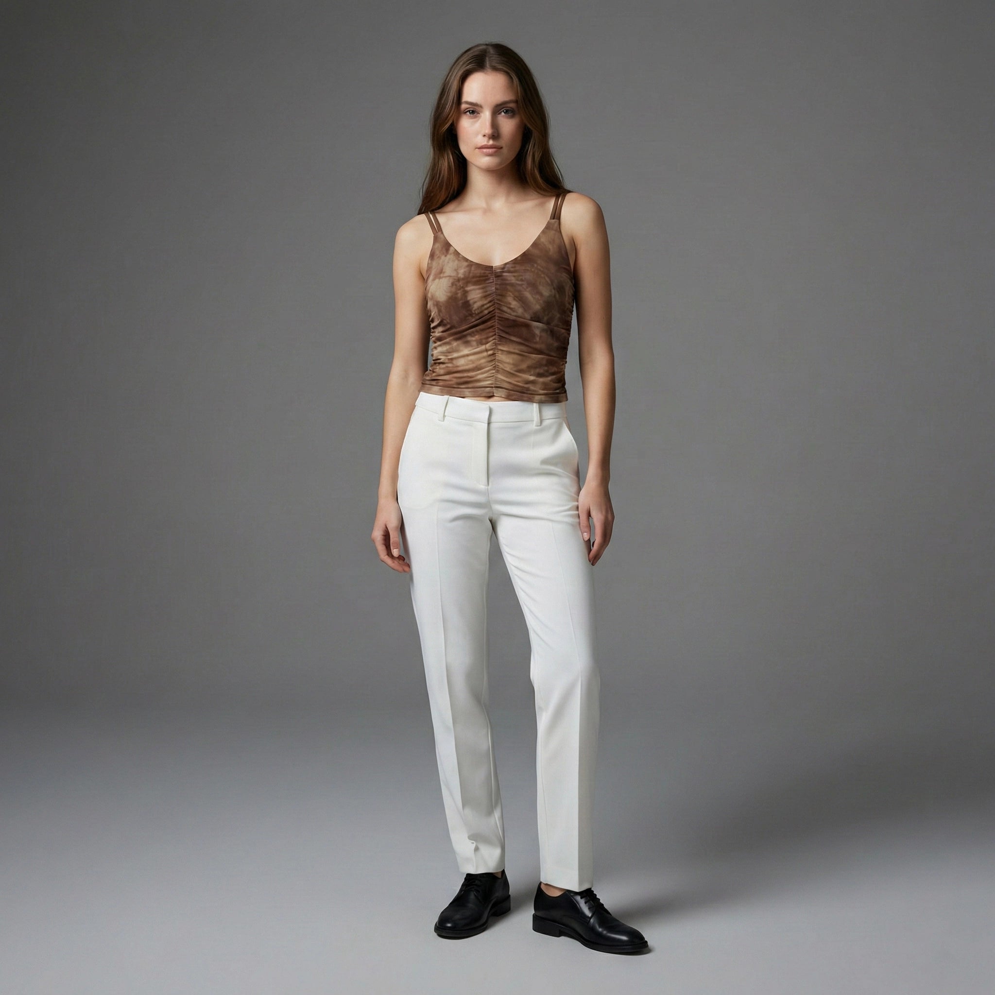Woman wearing a brown top and white pants against a gray background