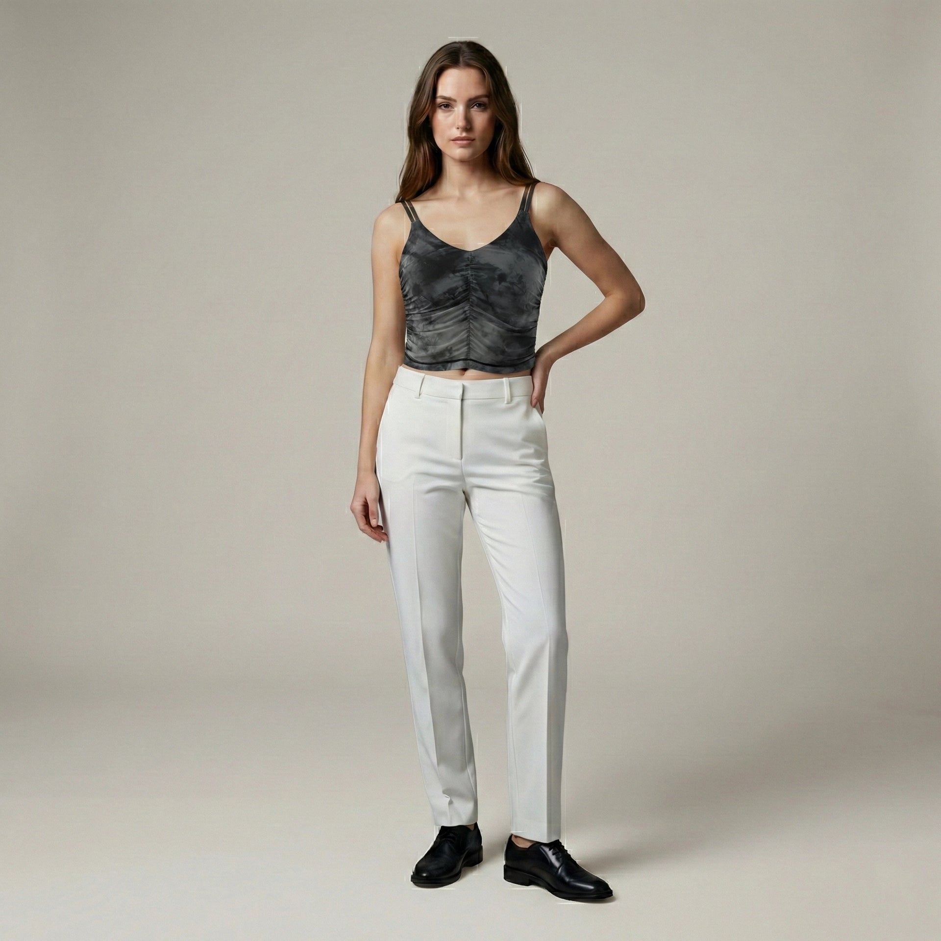Woman wearing a black sleeveless top and white pants against a plain background