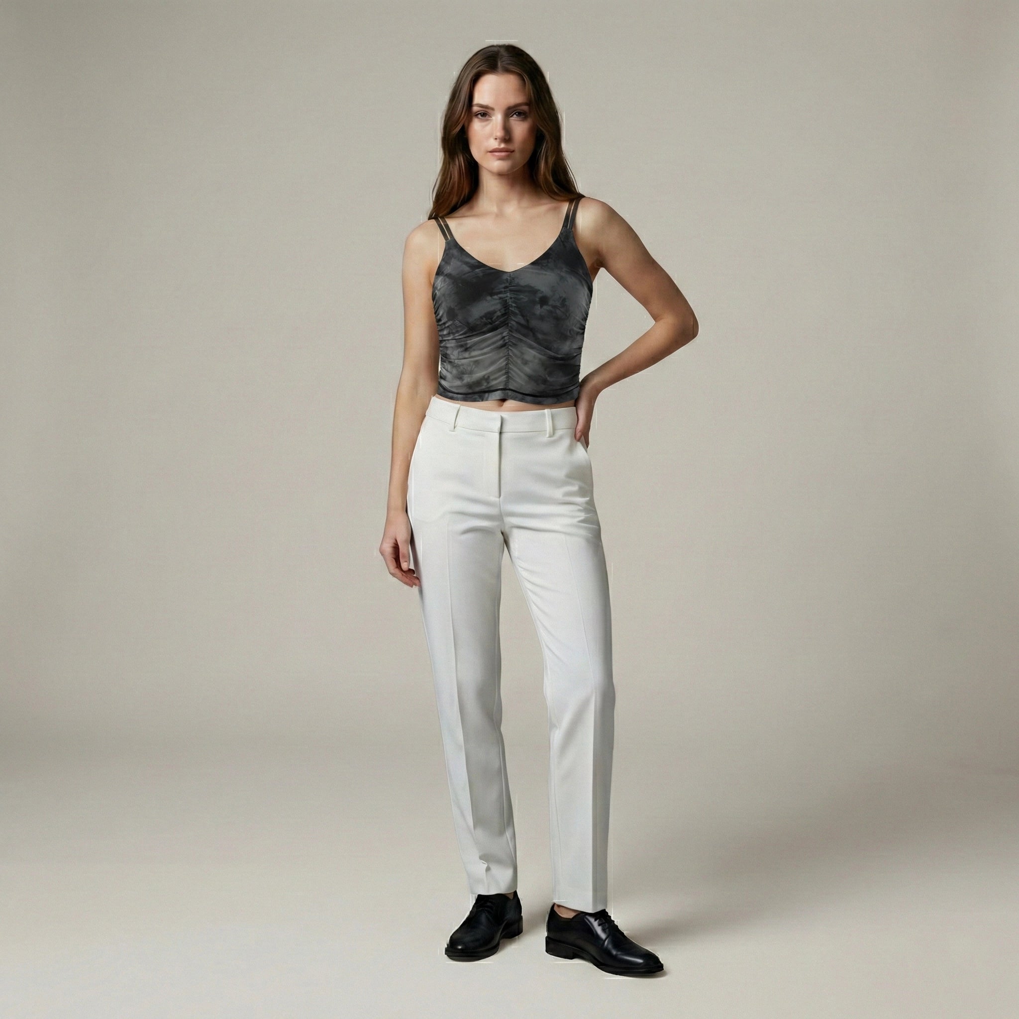 Woman wearing a black sleeveless top and white pants against a plain background