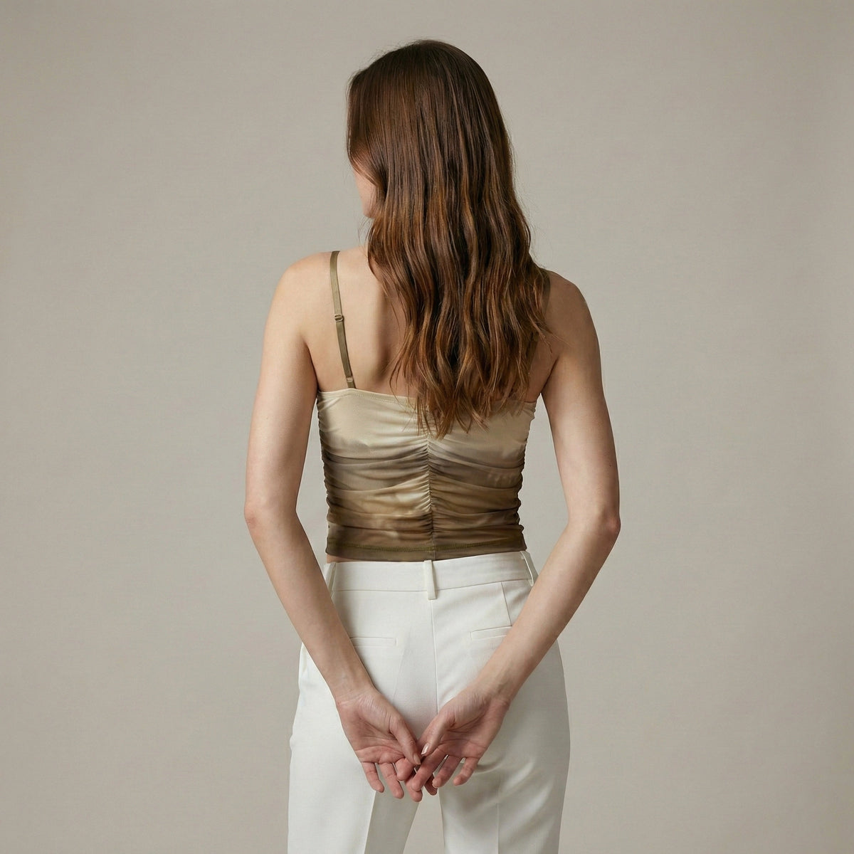 Woman wearing a brown strapless top and white pants against a beige background