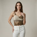 Woman wearing a gold tank top and white pants against a neutral background